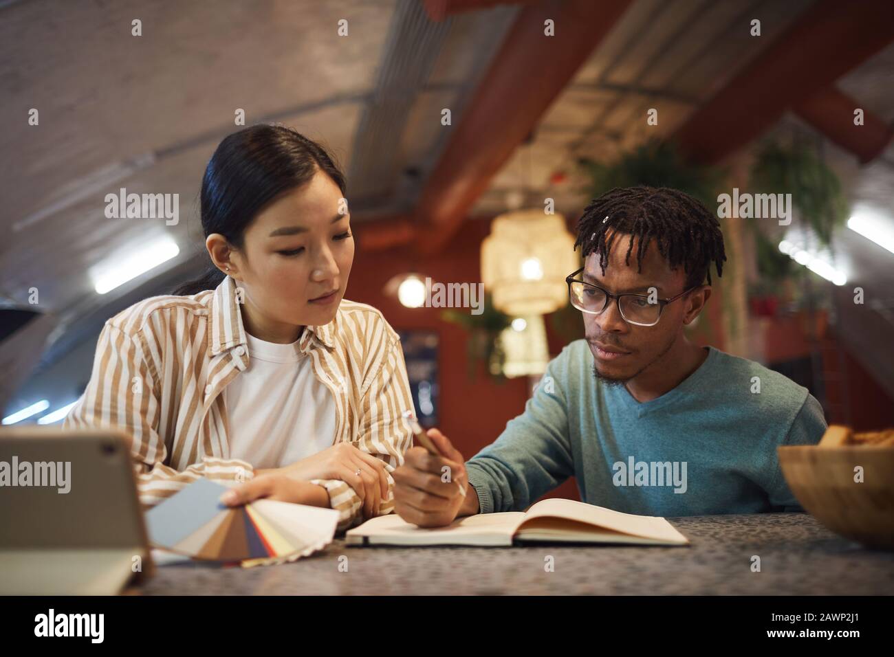 Portrait of two ethnic young people working on project together while sitting at table in office Stock Photo