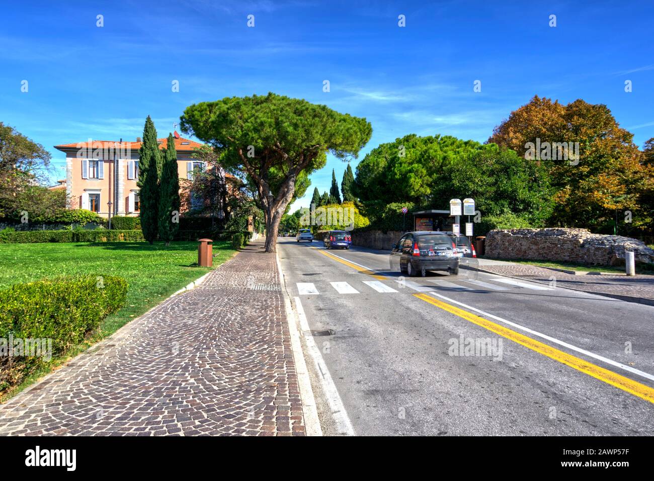 Rimini, Italy - October 20, 2019: Pretty pink house with attractive trees and vegetation, paved walkway and road with motion blurred cars Stock Photo