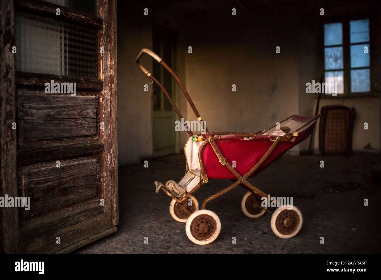 Old rusty baby carriage inside a building with weathered doors and windows Stock Photo