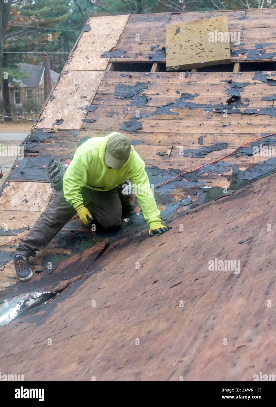 A roofer uses a tool to pull old nails from a rooftop, preparing it for