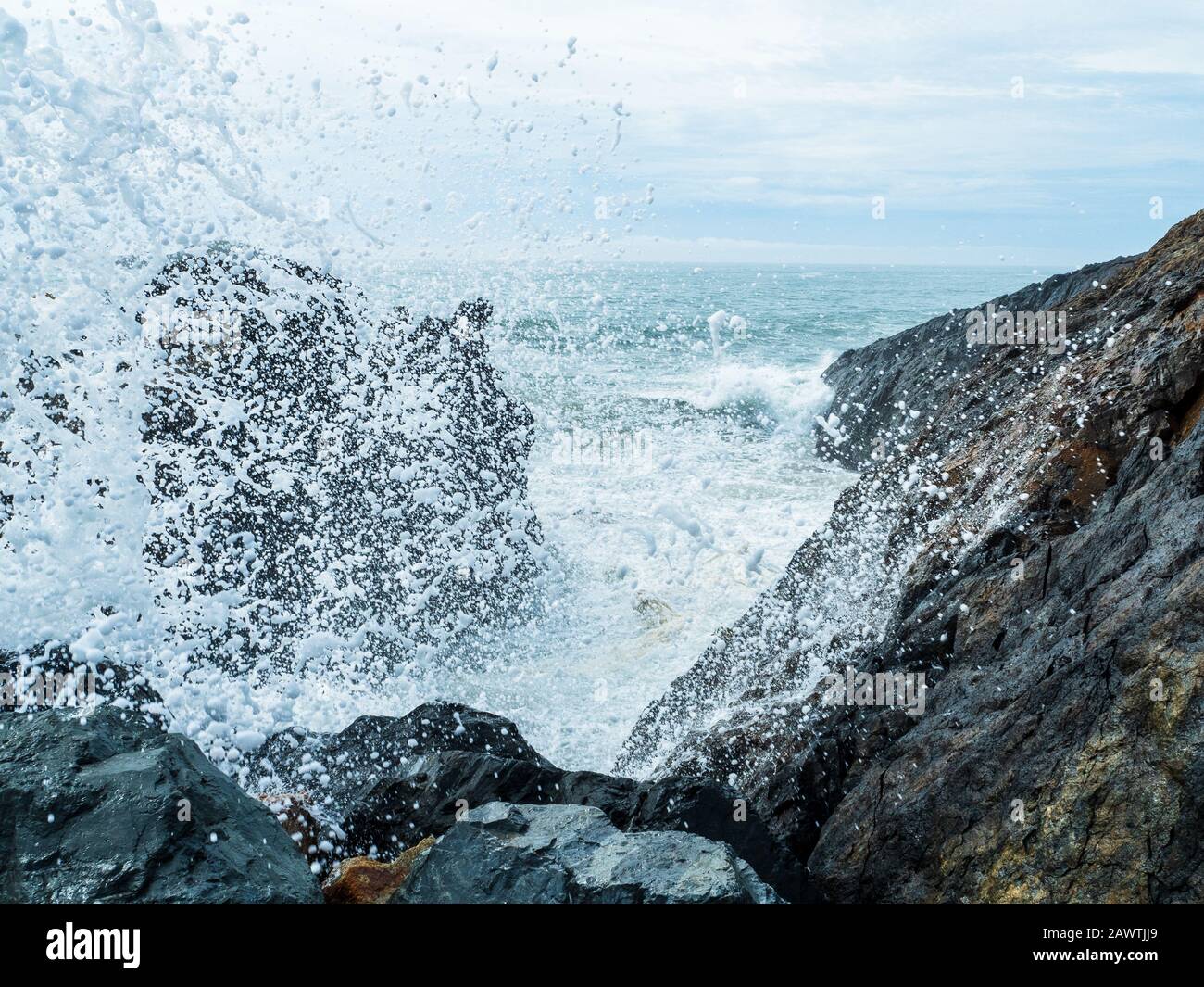 Frothy Foamy sea spray splashes up into the air, almost onto the lens as waves crash into rocks at the break wall, exploding water everywhere Stock Photo