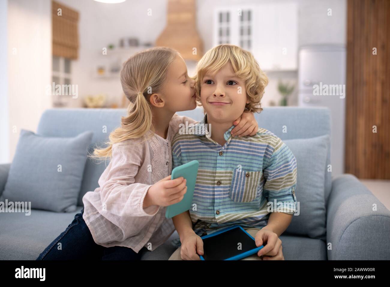 Blond girl holding smartphone and kissing boy Stock Photo