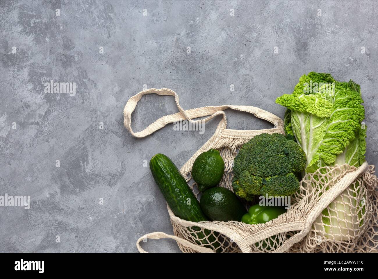 Green fresh vegetables in a string bag on a gray concrete background. Flat lay with copy space. Stock Photo