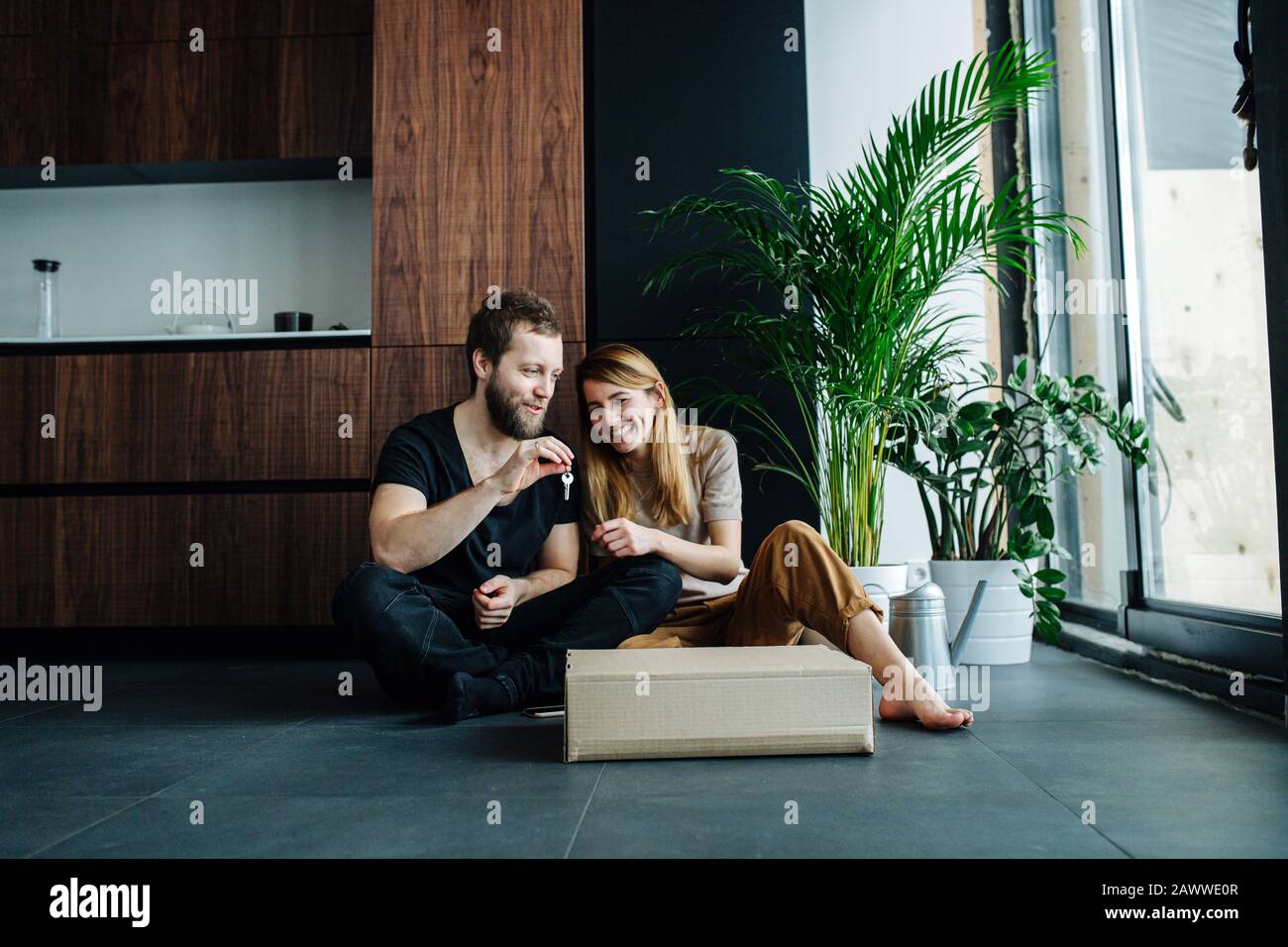 Longshot of a couple sitting on a floor with keys for their new apartment. Stock Photo