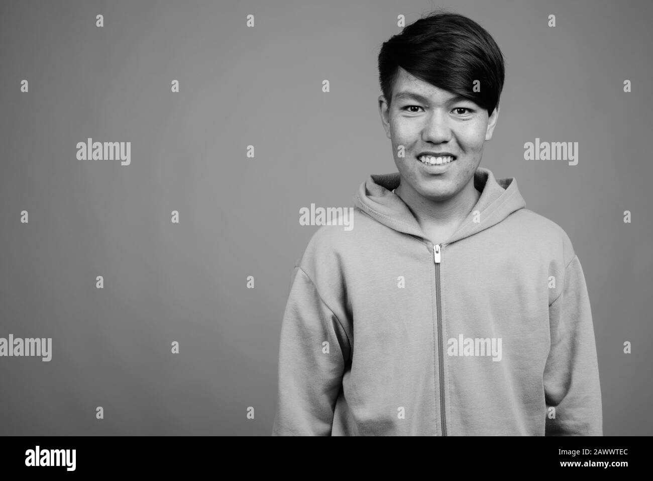 Young Asian teenage boy wearing hoodie against gray background Stock Photo