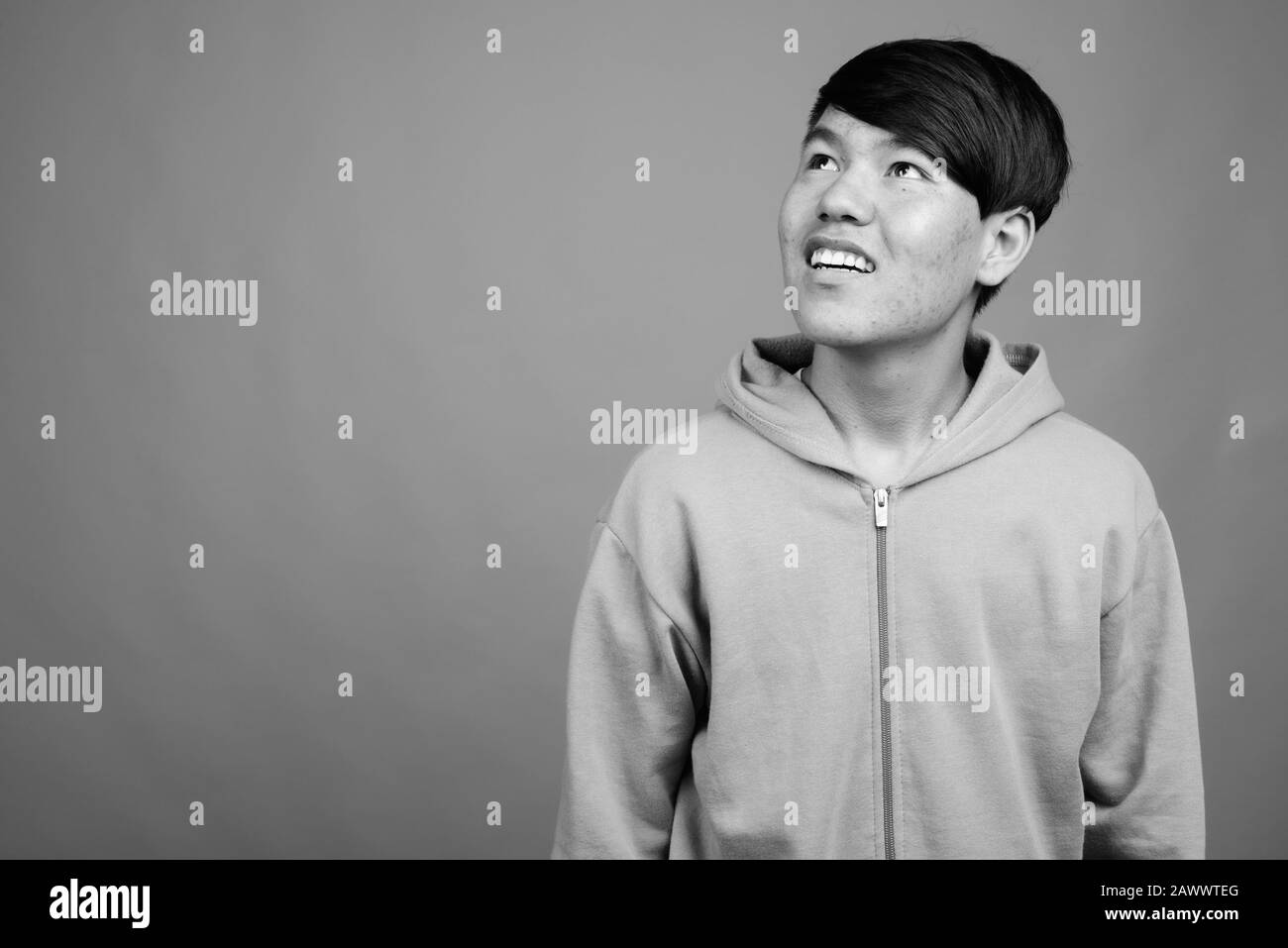 Young Asian teenage boy wearing hoodie against gray background Stock Photo