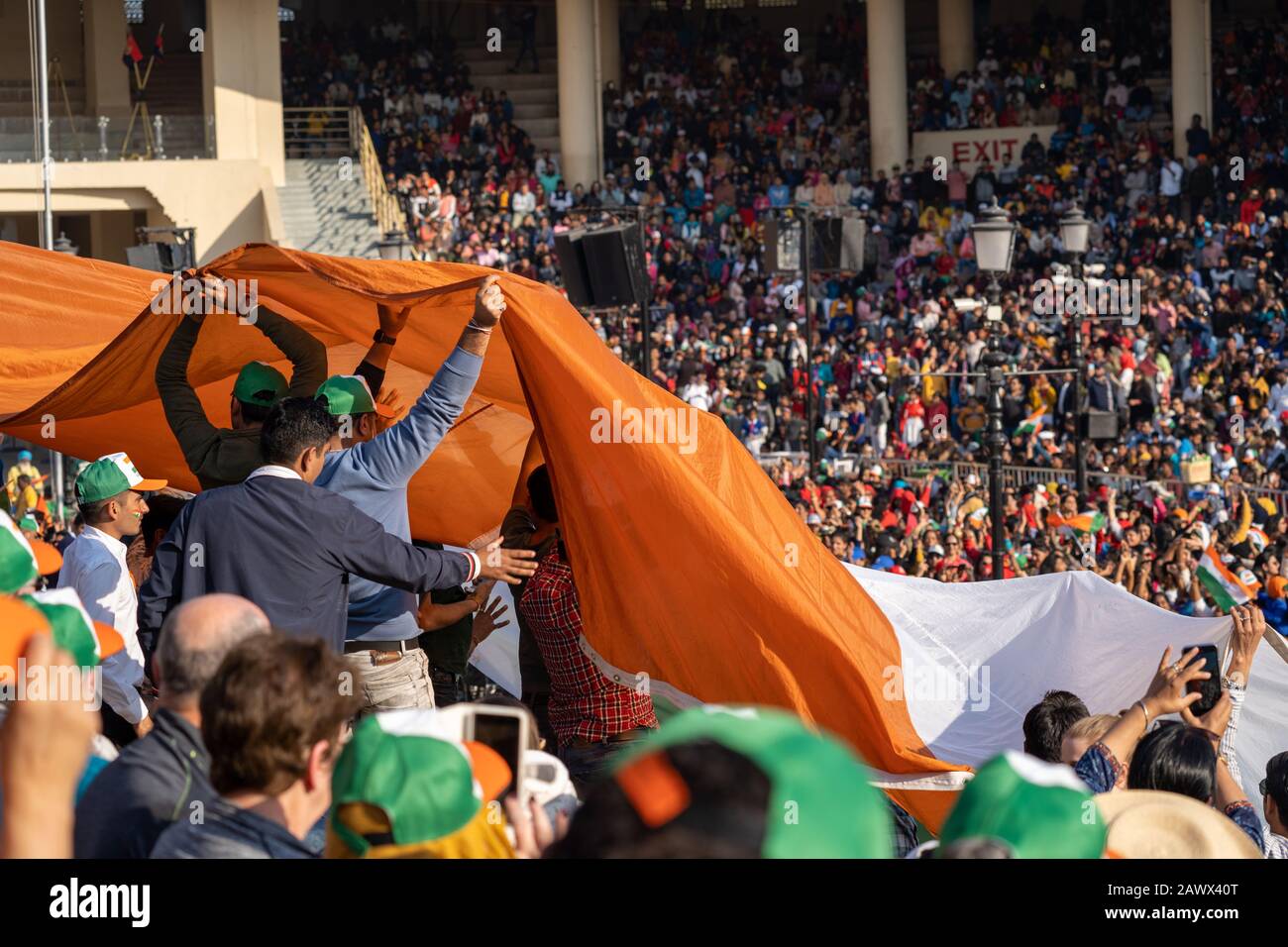 Amritsar, India - Febuary 8, 2020: Crowds in the stadium seating pass up and hold an Indian Flag in preparation of the Wagah Border Closing ceremony w Stock Photo