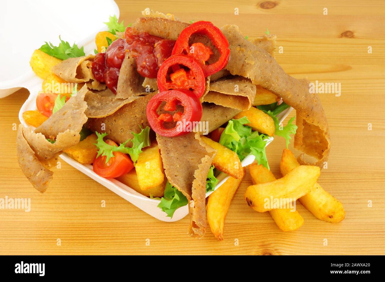 Doner kebab meat and chips with salad and chilli sauce in a take away tray on a wood background Stock Photo