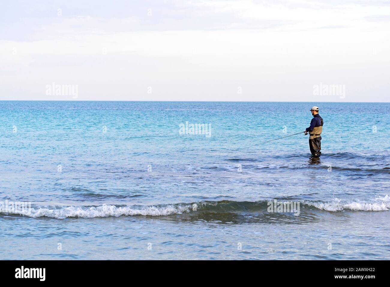 Fisherman standing at the seashore cast the fishimg rod. Sportsman holds a fishing rod and reel in a hooked fish. Spin Fishing hobby catching a fish a Stock Photo