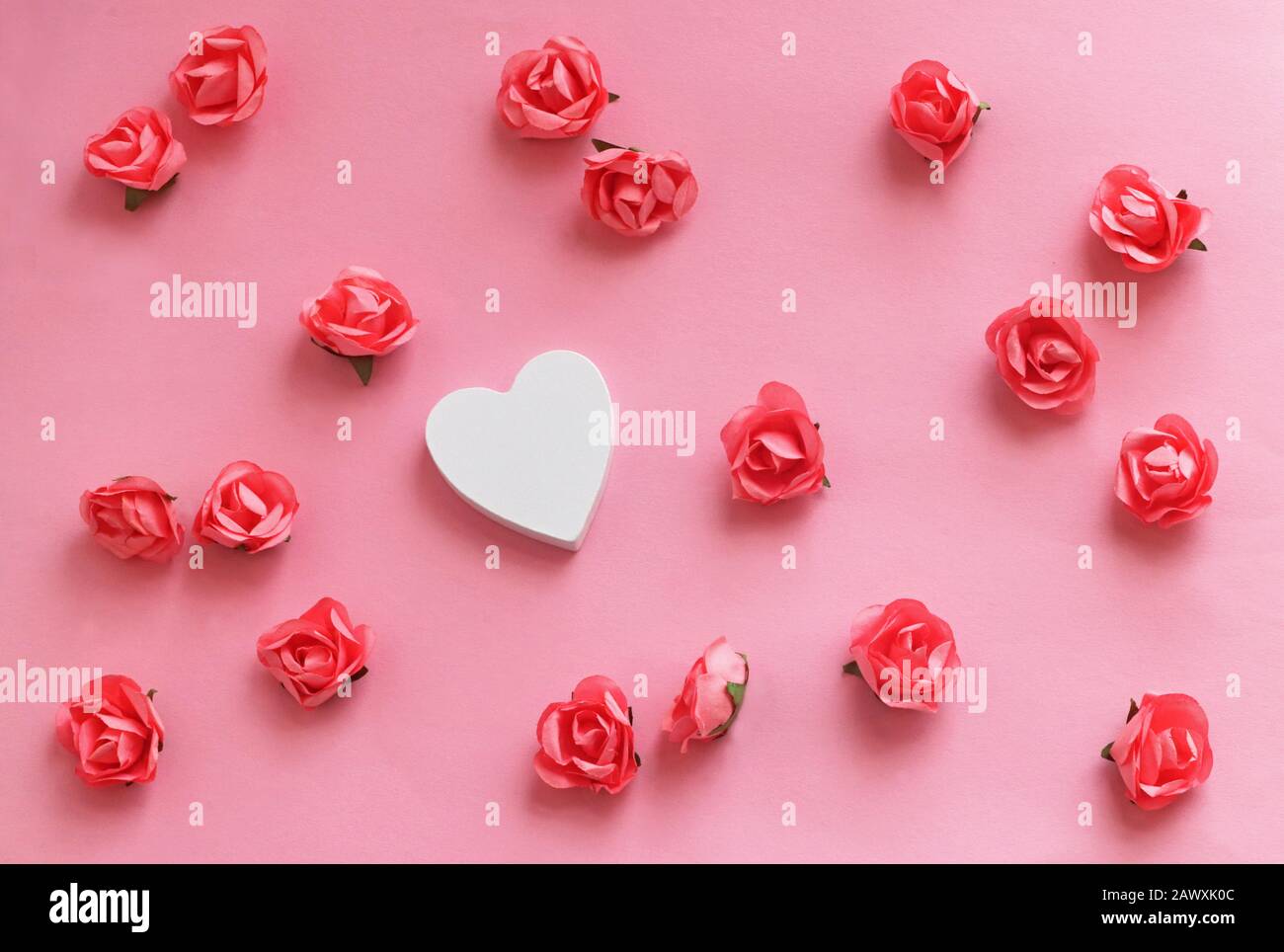 romantic background with a white wooden heart lying between pink paper roses on a pink table Stock Photo