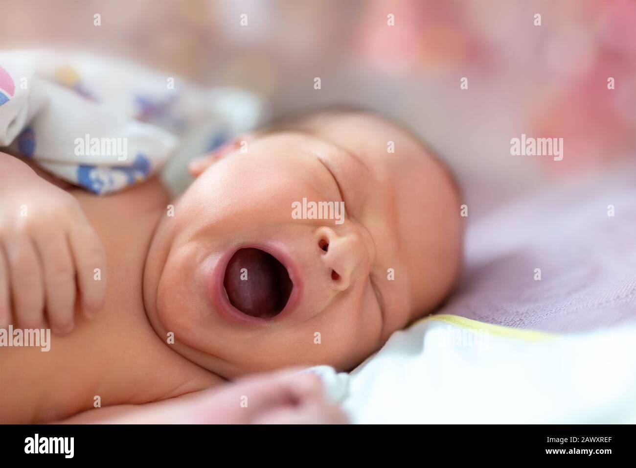 One week newborn adorable innocent baby lying at baycot and funny yawning.Portrait of sleepy caucasian infant tired child on bed. Wide open mouth and Stock Photo