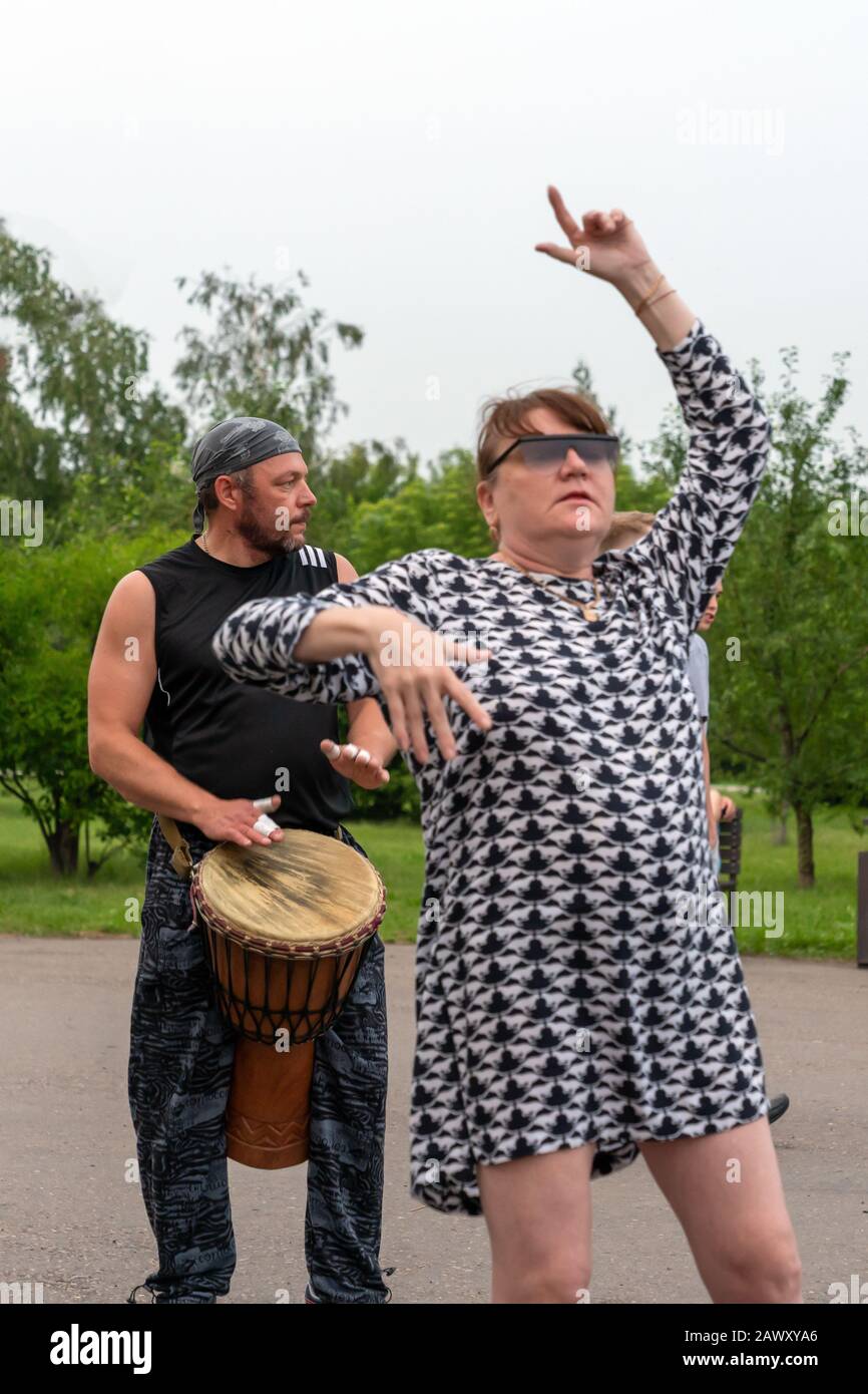 Krasnoyarsk, Russia, June 30, 2019: an adult female freak in glasses dances to African Tam Tam djembe drums in a public Park. party, vertical photo. Stock Photo