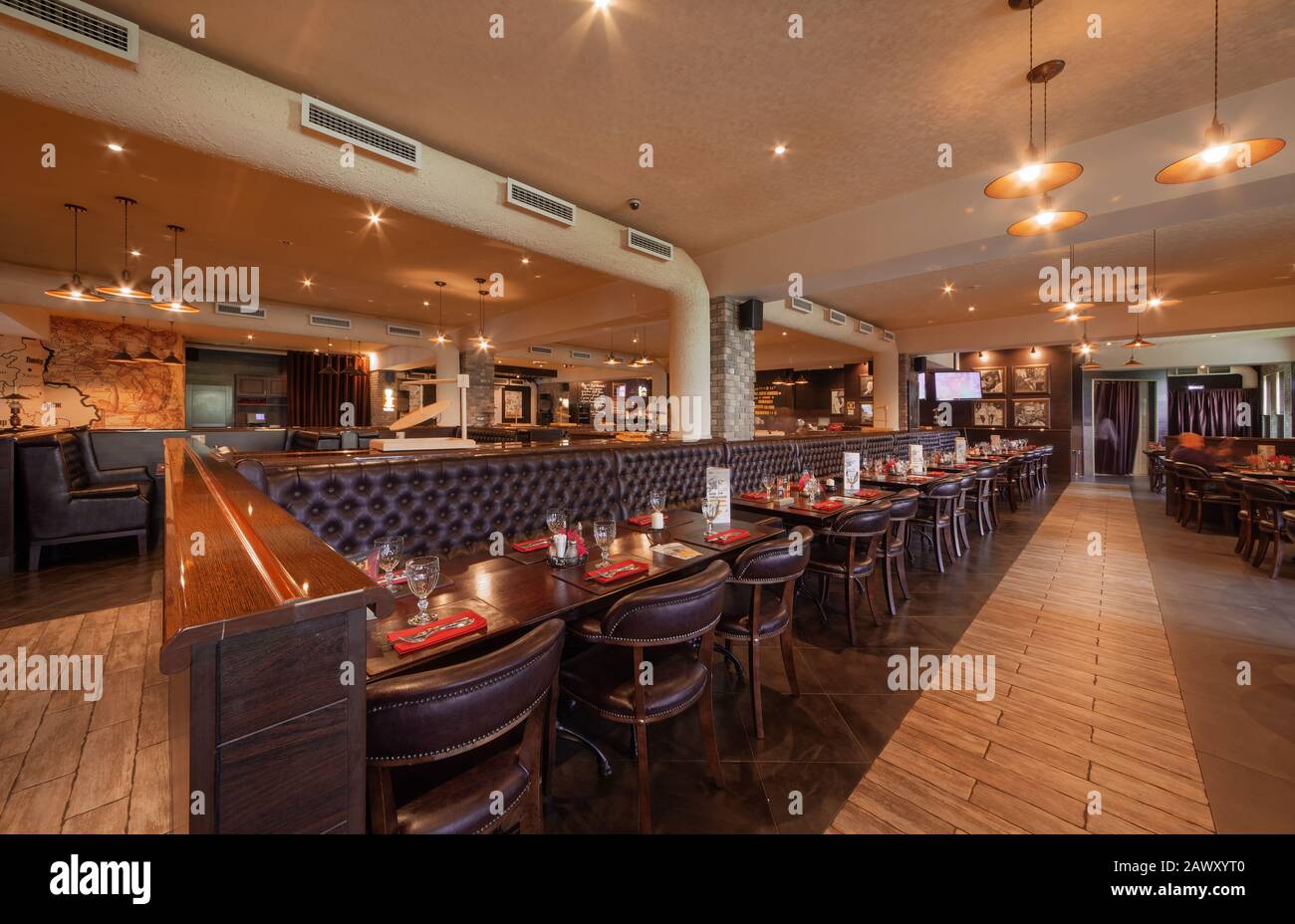 MOSCOW - SEPTEMBER 2014: The interior of a large beer restaurant 'Yan Primus'. Long brown leather sofa for several tables in the center of the hall Stock Photo