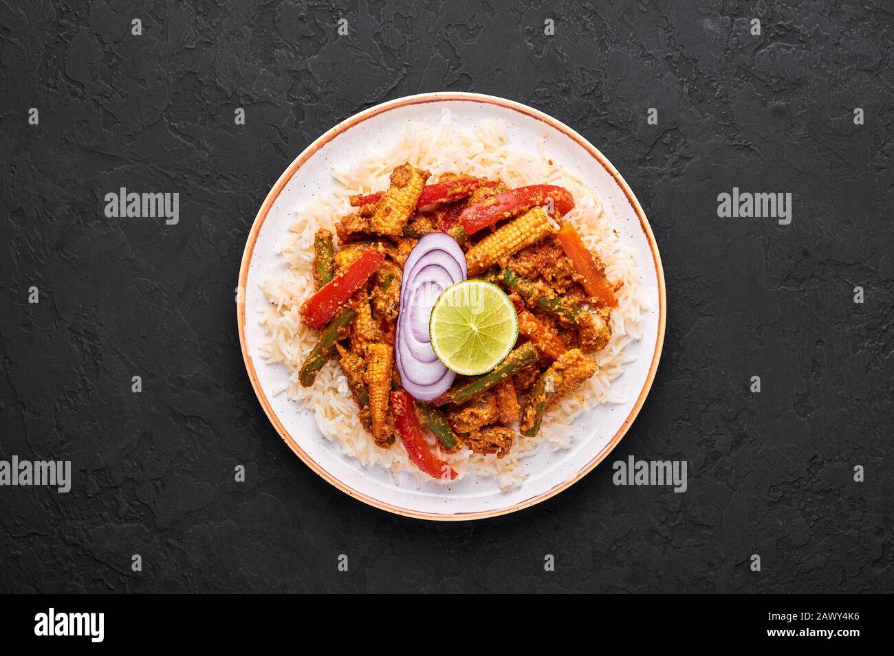 Vegetable Jalfrezi with basmati rice in white plate at black slate background. Jalfrezi is Indian Cuisine dish with stir fried vegetables and tomato-n Stock Photo