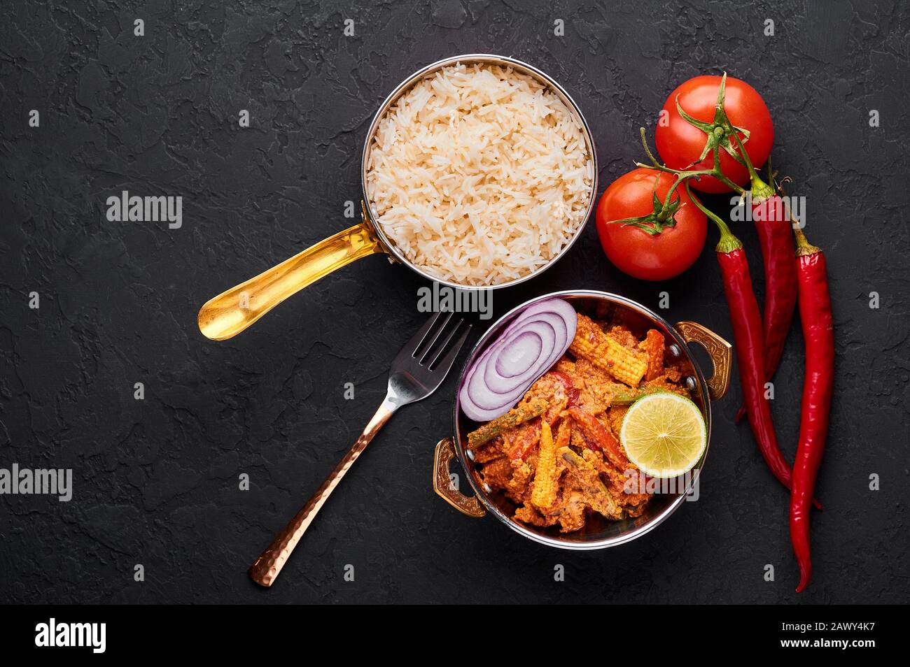 Vegetable Jalfrezi in copper kadai with basmati rice at black slate background. Jalfrezi is Indian Cuisine dish with stir fried vegetables and tomato- Stock Photo