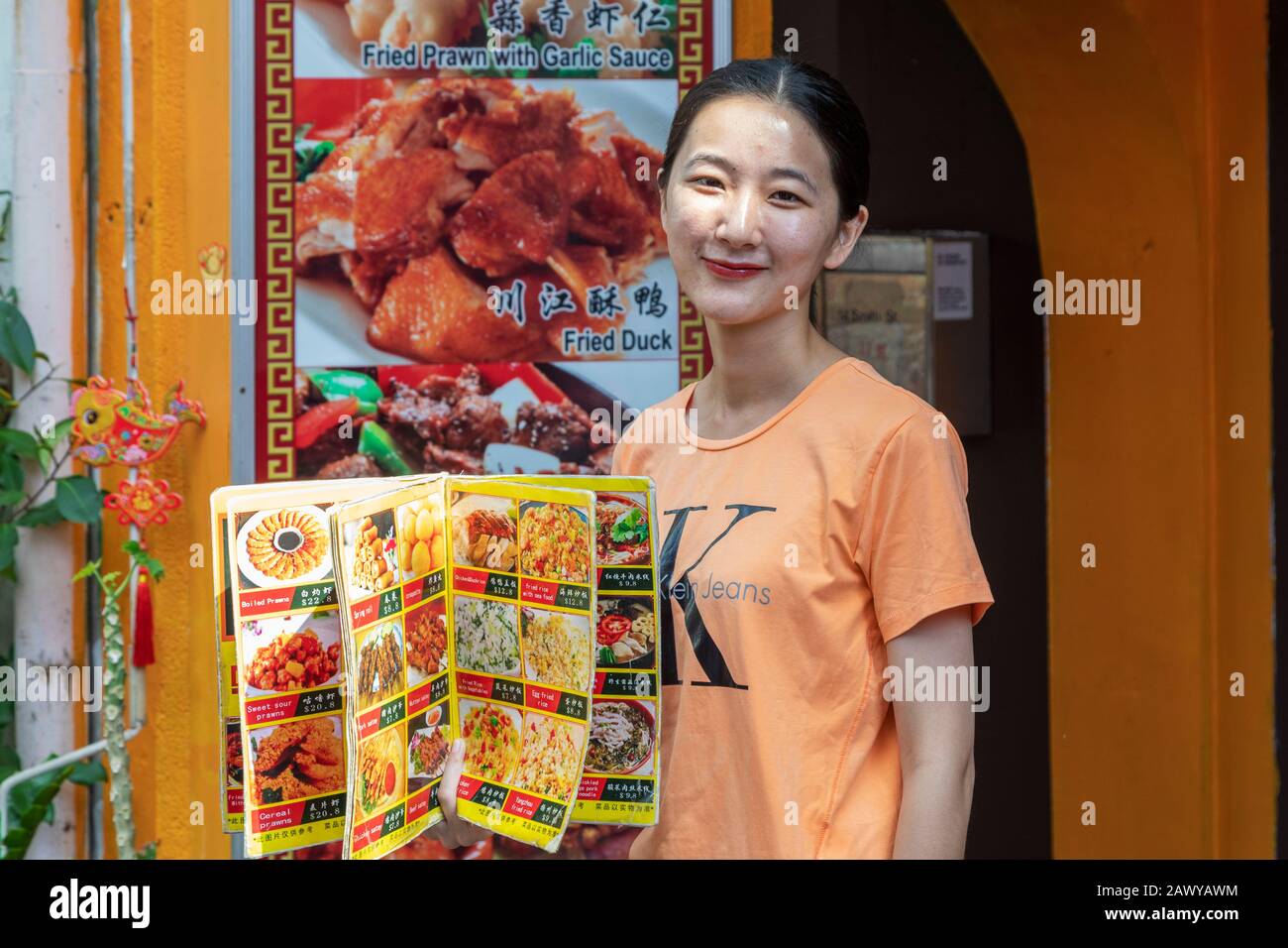 Young woman working as a waitress displaying a menu from the restaurant she works in, Chinatown, Singapore, Asia Stock Photo