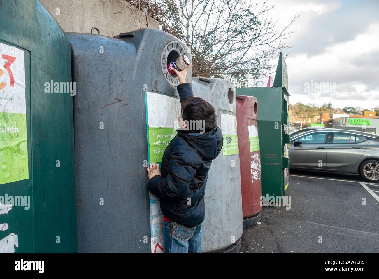 A young boy puts an empty glass jar into a bottle bank. The glass will be recycled. Stock Photo