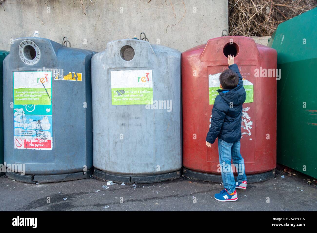 A young boy puts an empty glass jar into a bottle bank. The glass will be recycled. Stock Photo