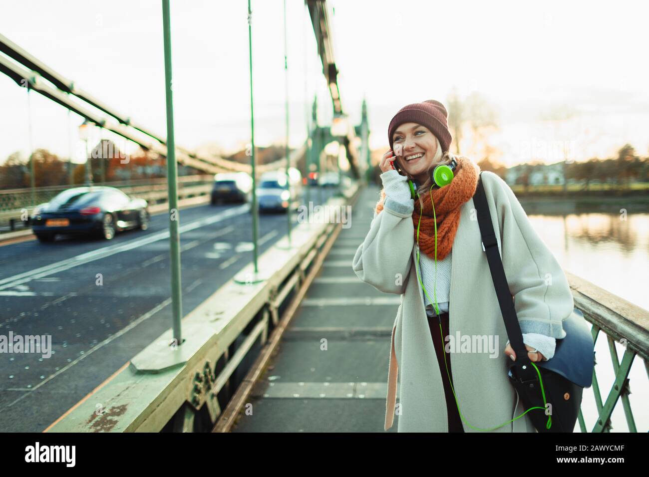 Young woman in stocking cap and scarf talking on smart phone on bridge Stock Photo