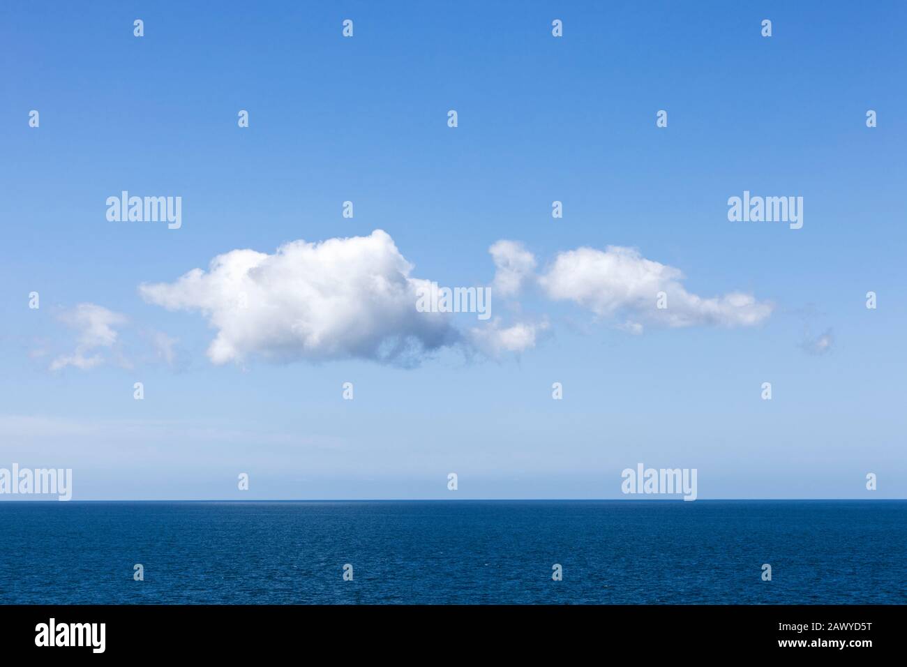 Cumulus clouds forming in a clear blue sky over a calm ocean horizon Stock Photo