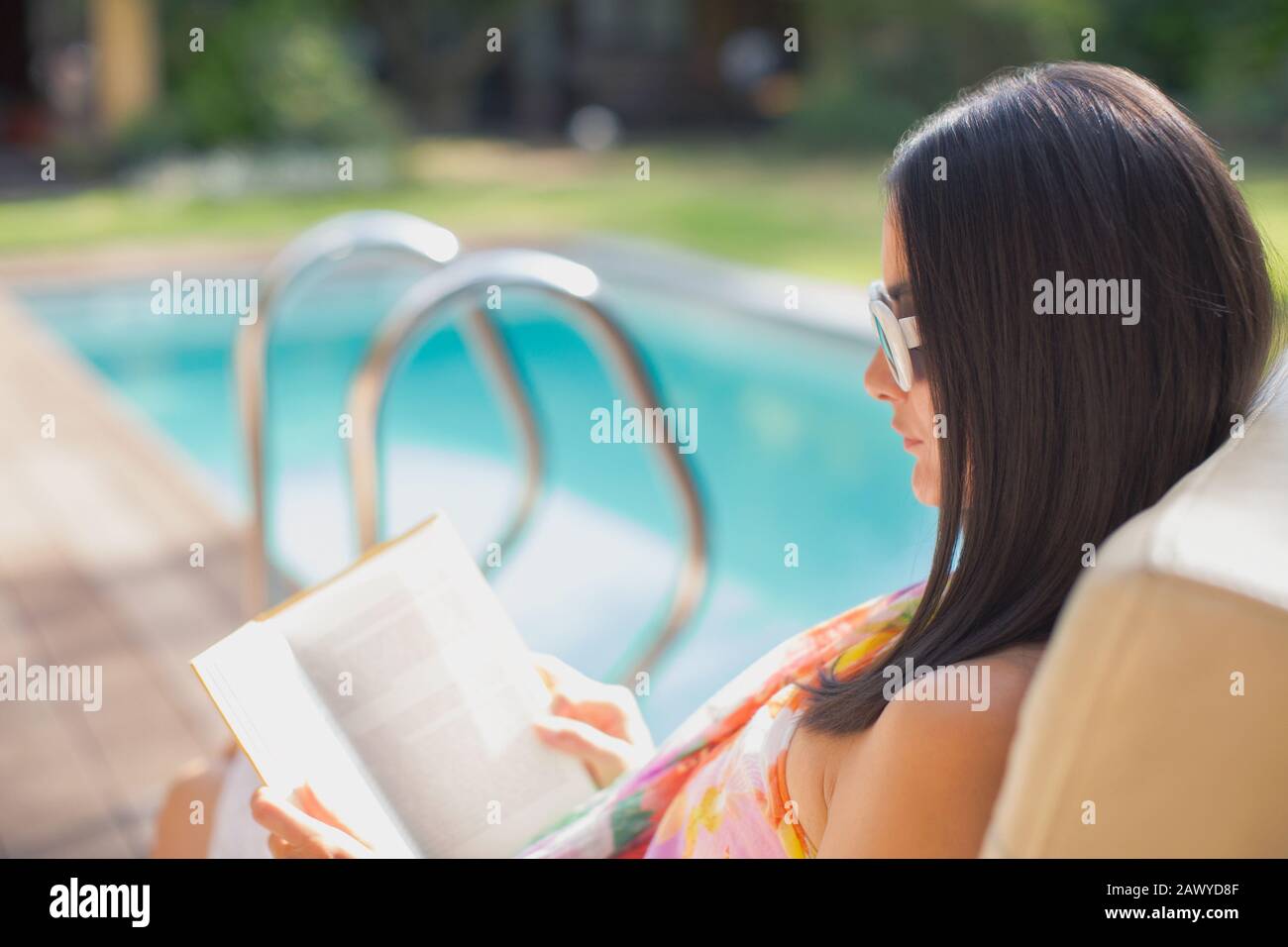 Woman reading book at sunny summer poolside Stock Photo