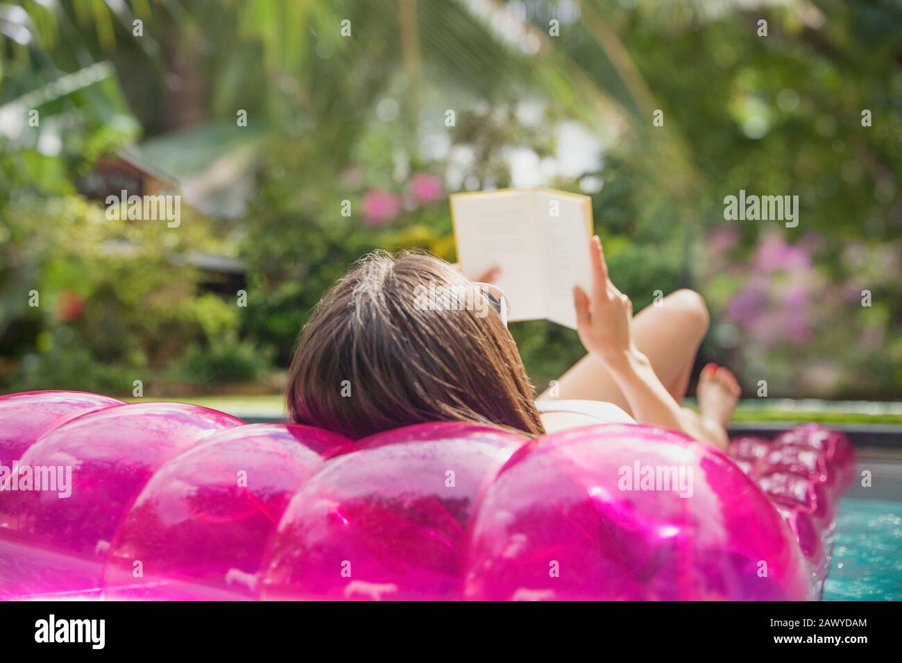 Woman relaxing, reading book on inflatable raft in swimming pool Stock Photo