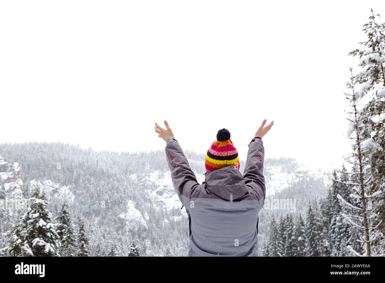 Young female with hands raised towards the sky on winter snowy day. Freedom concept. Place for text. Stock Photo