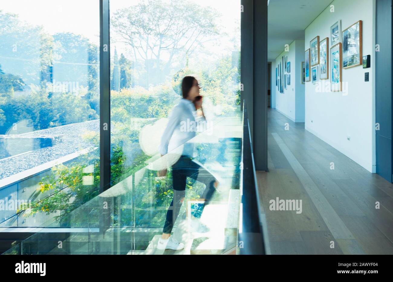 Woman ascending stairs in sunny modern, luxury home Stock Photo