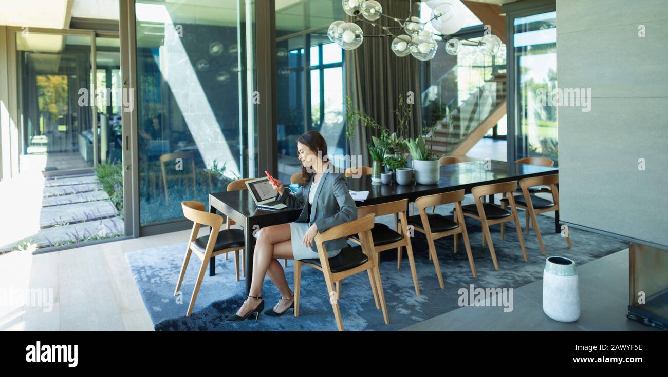 Businesswoman working from home, using smart phone at modern dining table Stock Photo