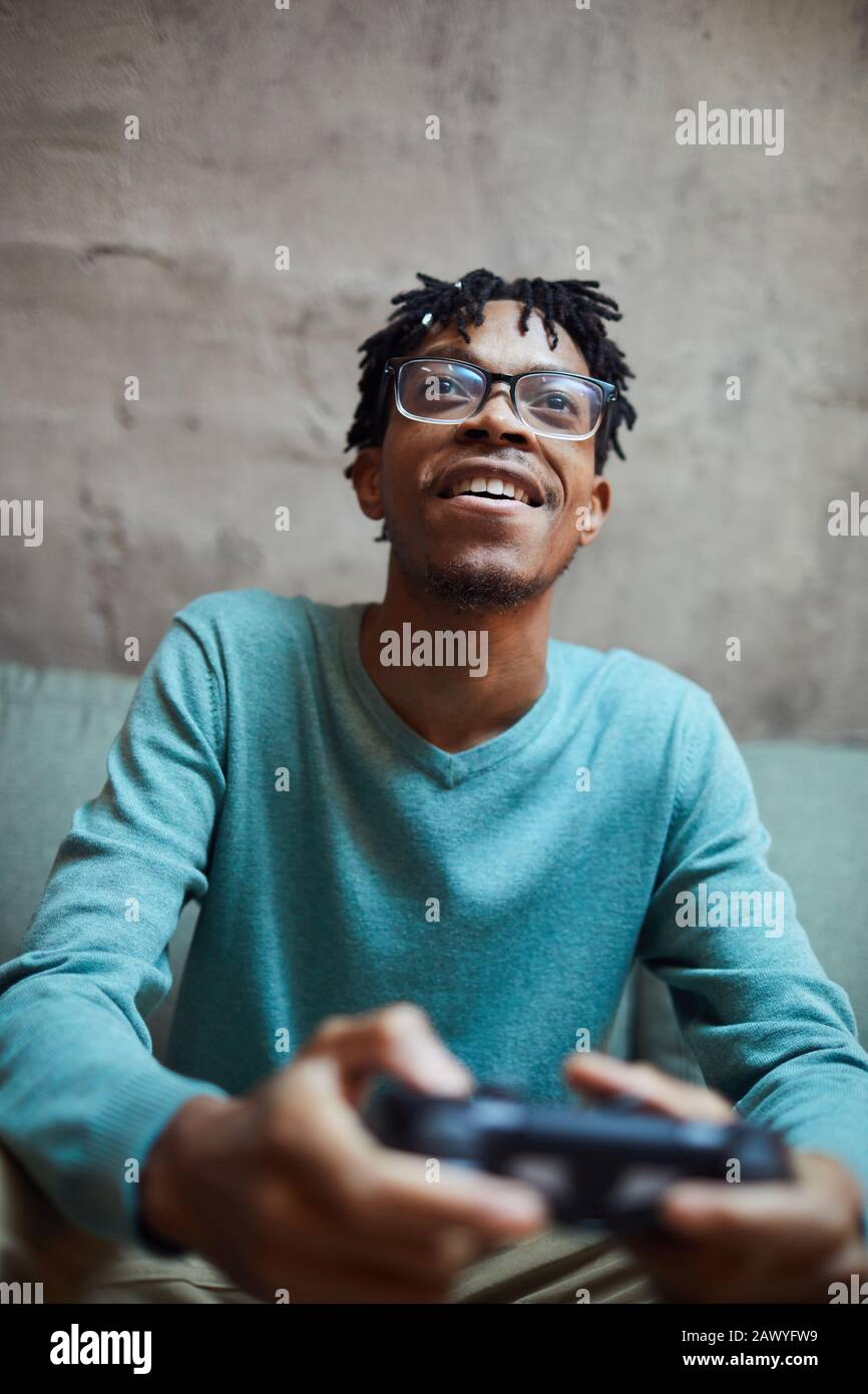 Low angle portrait of smiling African-American man playing videogames via gaming console Stock Photo