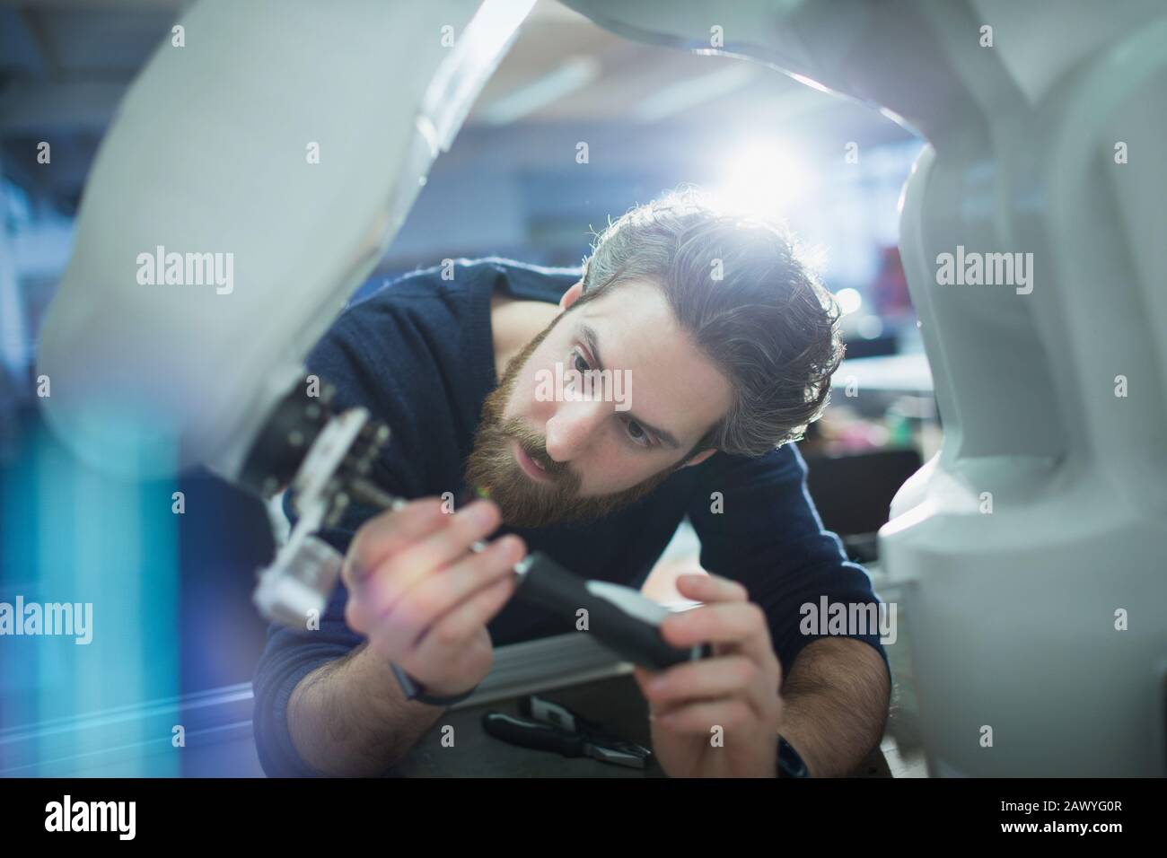 Focused male engineer with screwdriver fixing robotic arm Stock Photo