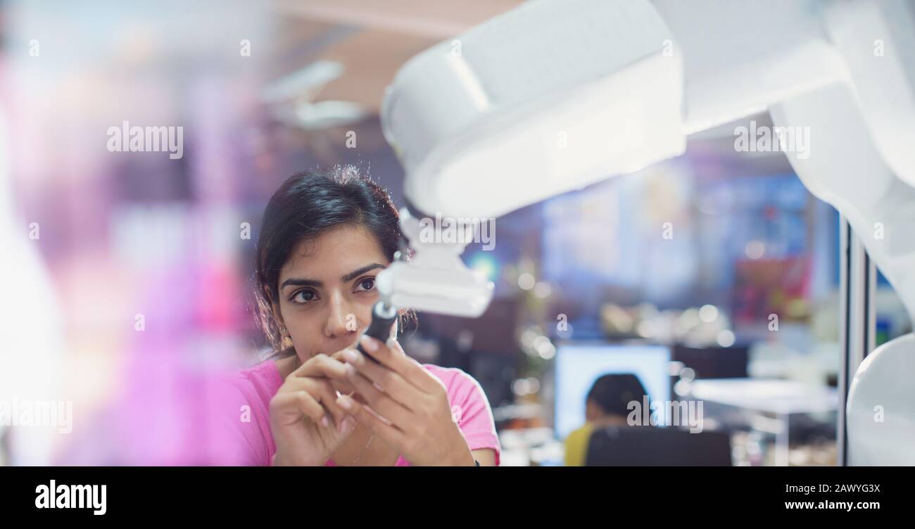 Focused female engineer with screwdriver fixing robotic arm Stock Photo