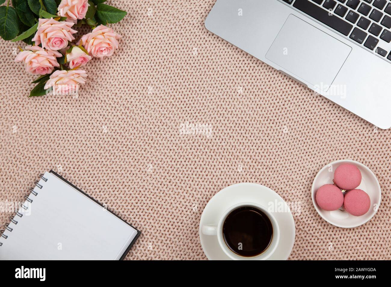 Work from home concept. Modern female working space, top view. Laptop, coffee, cakes, roses, notebook on knitted blanket, copy space, flat lay. Deskto Stock Photo