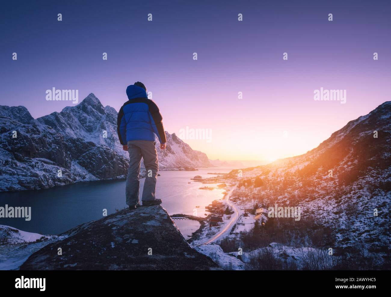 Man is standing on the mountain peak against snowy fjord Stock Photo