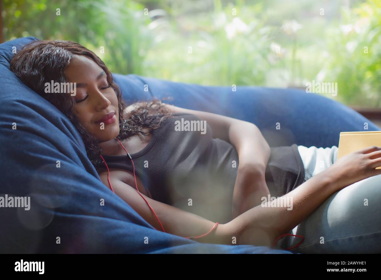 Serene young woman with headphones listening to music in beanbag chair Stock Photo