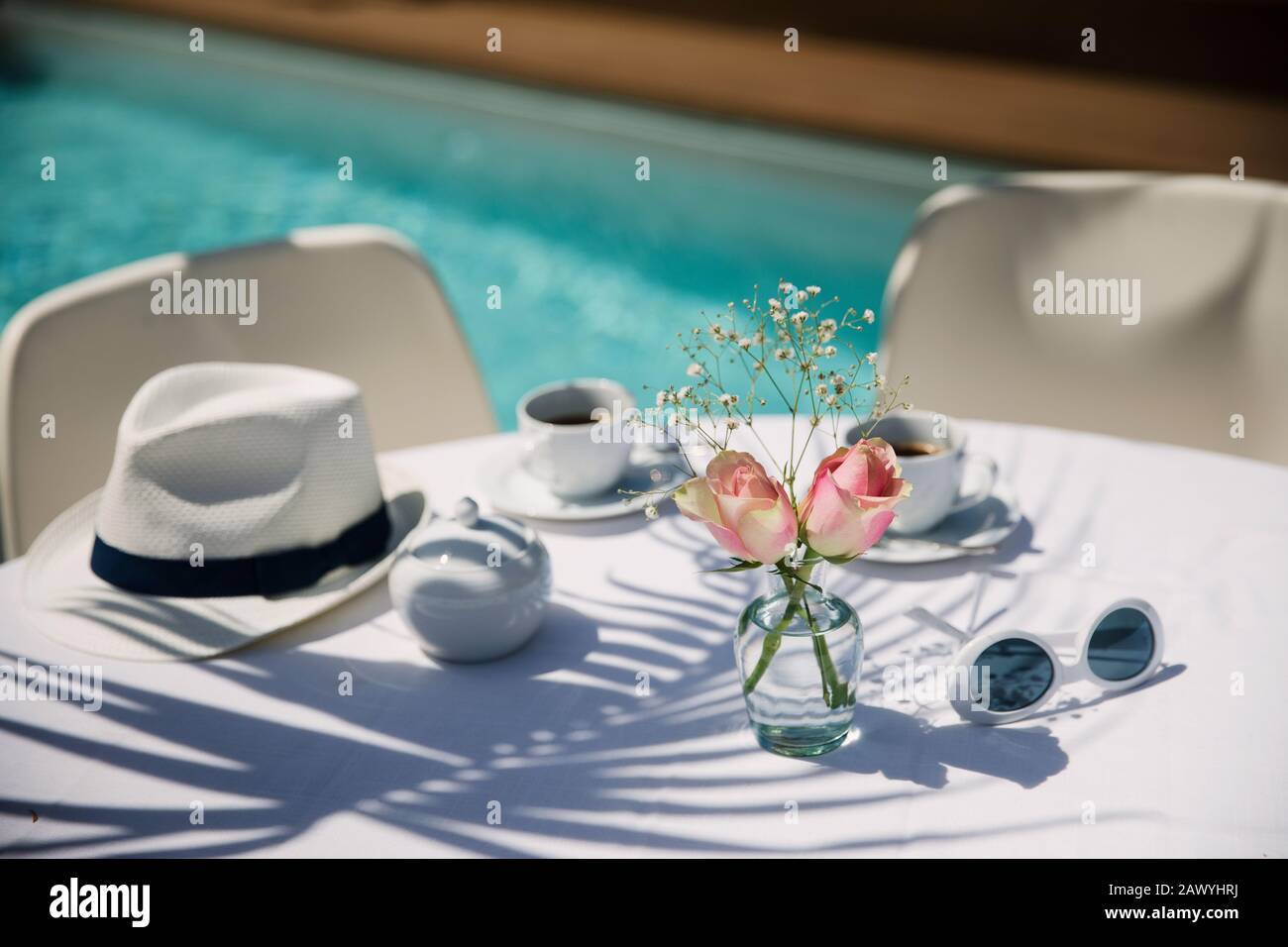 Roses and coffee on sunny poolside patio table Stock Photo