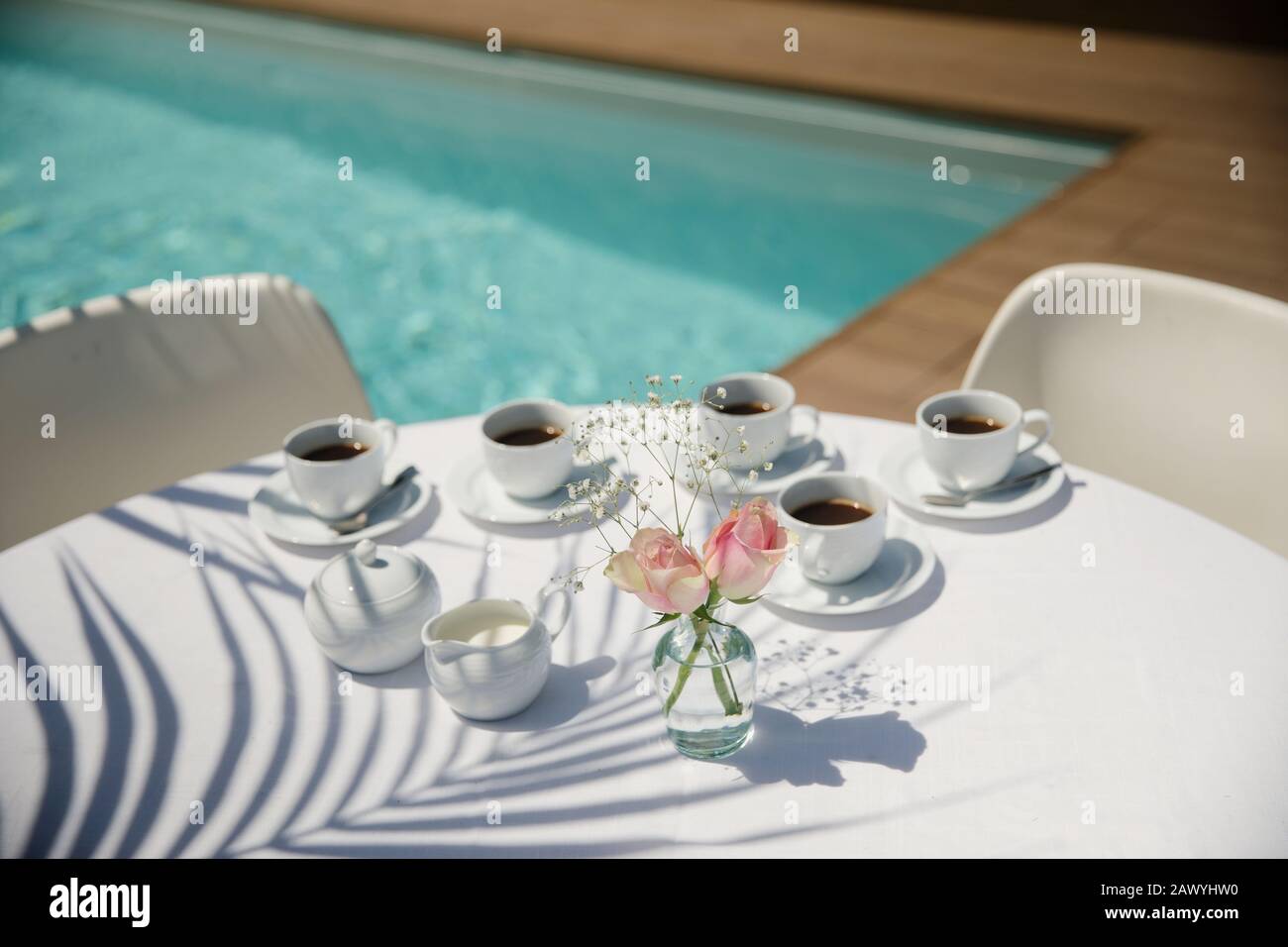 Coffee cups and roses on sunny summer poolside patio table Stock Photo