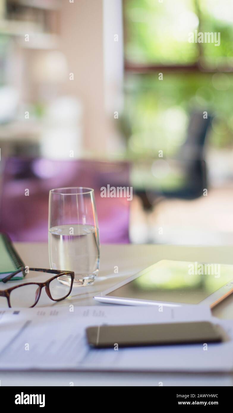 Water glass and eyeglasses on table with paperwork Stock Photo