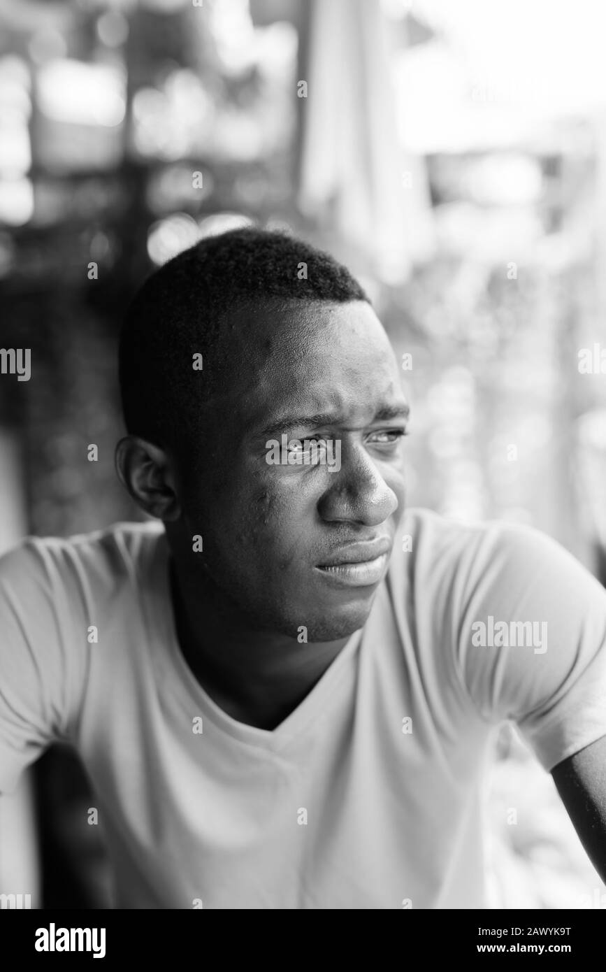 Face of young black African man thinking while looking at distance in the peaceful garden outdoors Stock Photo