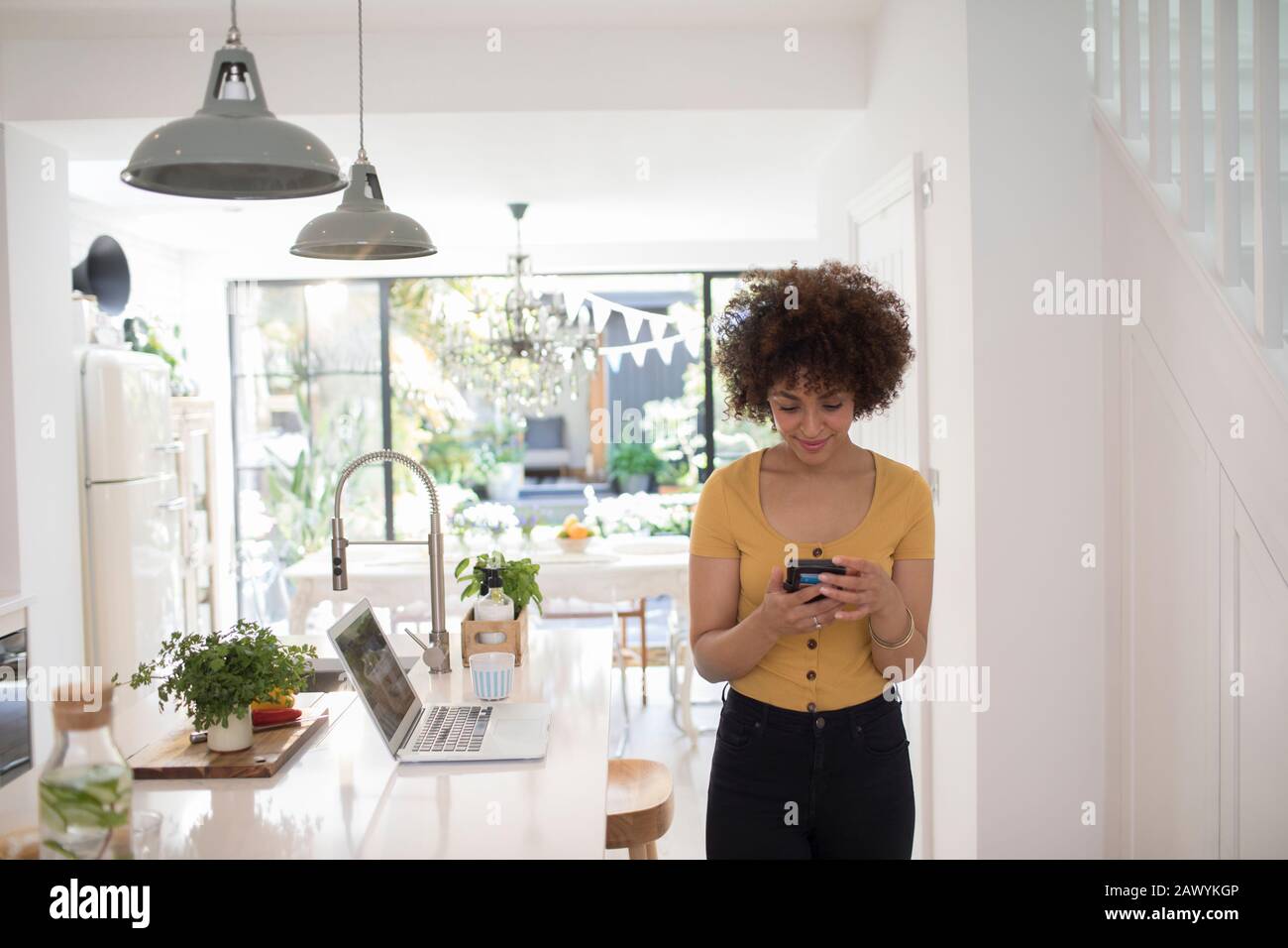 Young female freelancer using smart phone in kitchen Stock Photo