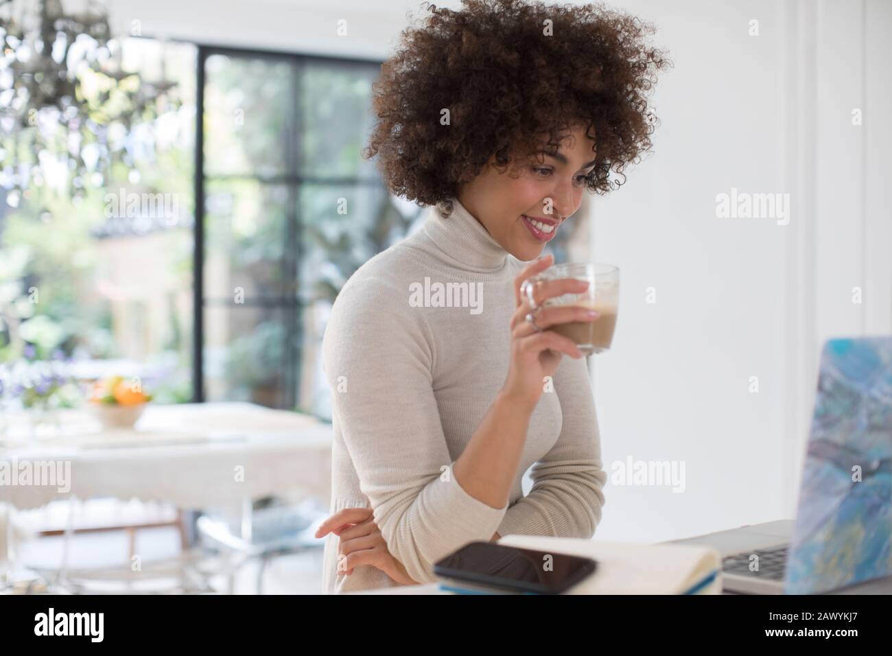 Young female freelancer drinking coffee at laptop Stock Photo