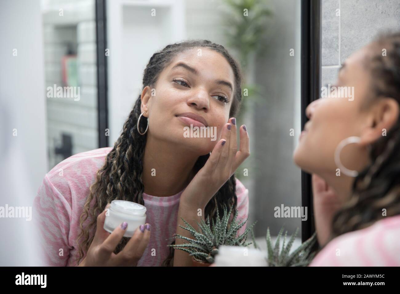 Beautiful young woman applying moisturizer in bathroom mirror Stock Photo
