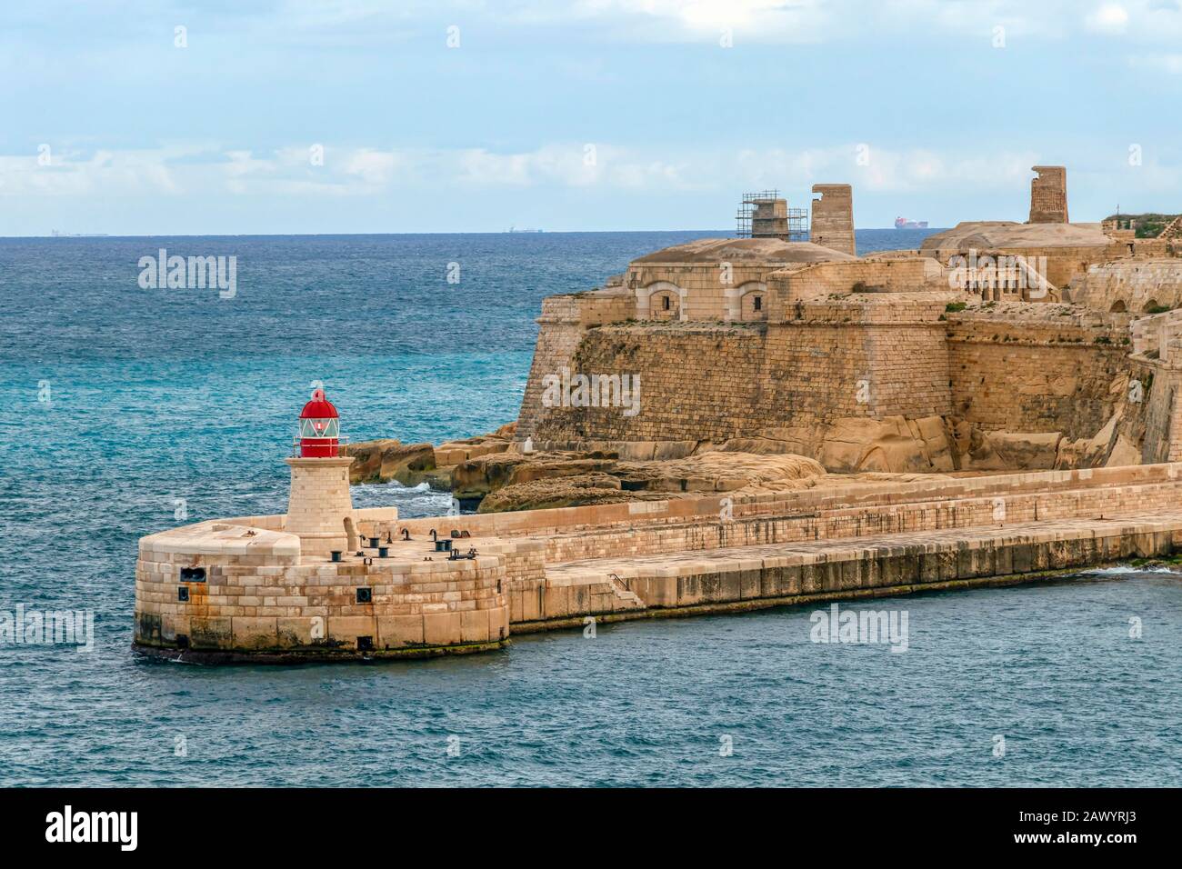 Red old Lighthouse in Grand Harbour and breakwater bridge, Fort Ricasoli from Valletta in Malta, Mediterranean sea region island Stock Photo