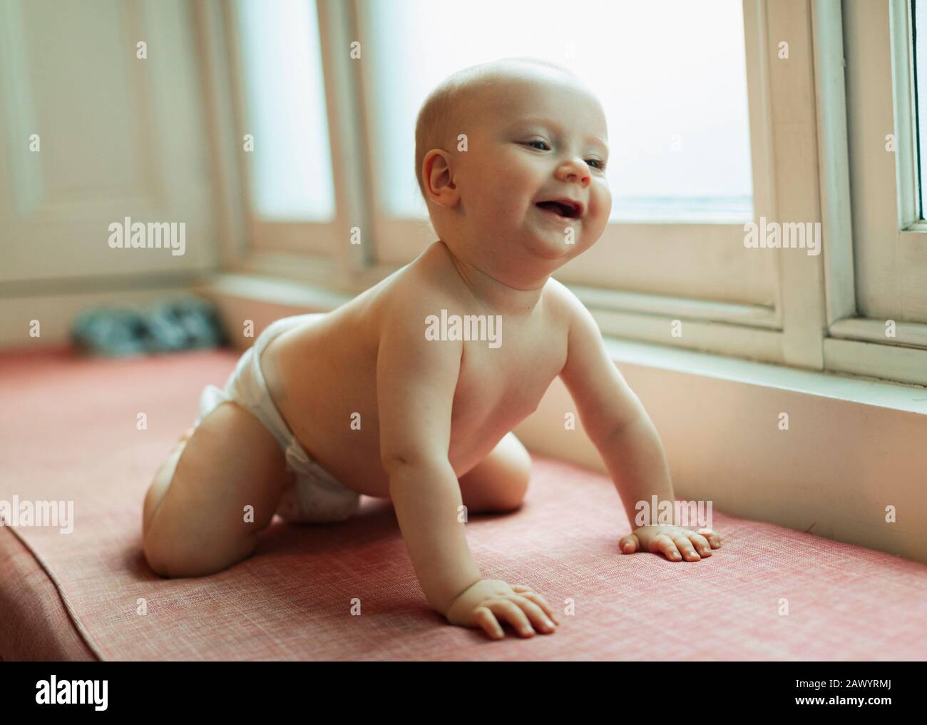 Cute baby girl in diaper laughing on window seat Stock Photo