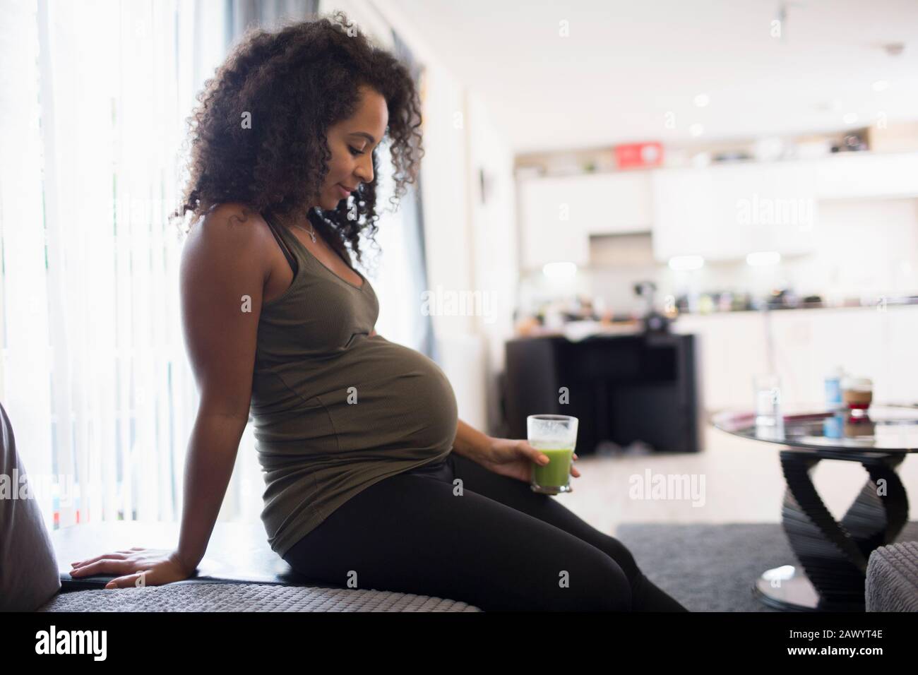 Young pregnant woman drinking green smoothie in living room Stock Photo