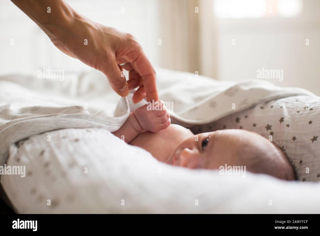 Mother holding hands with newborn baby boy laying in Stock