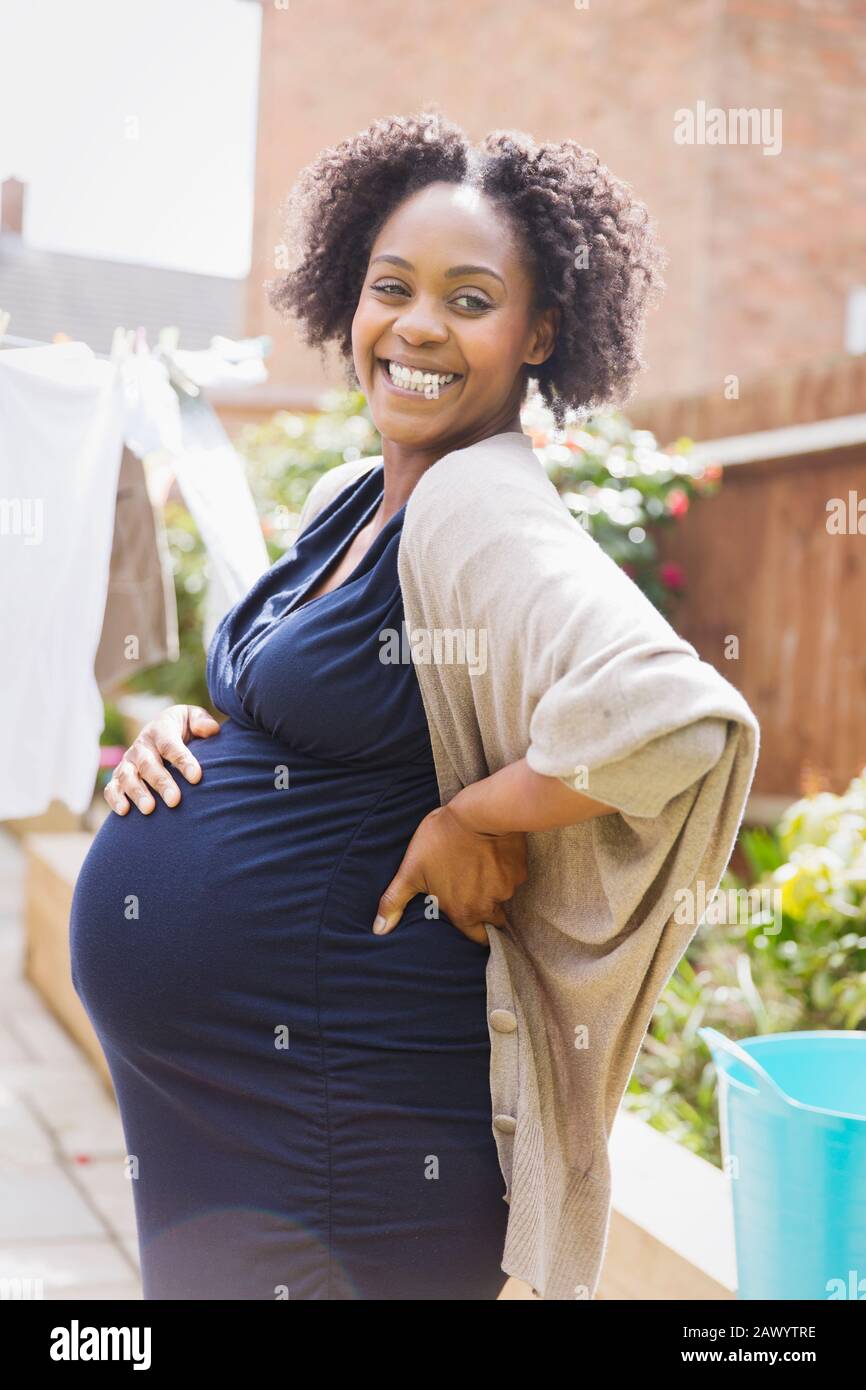 Portrait happy pregnant woman in sunny garden Stock Photo
