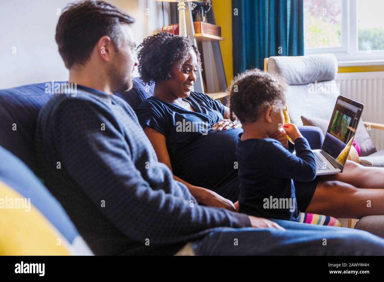 Pregnant family using laptop on sofa Stock Photo