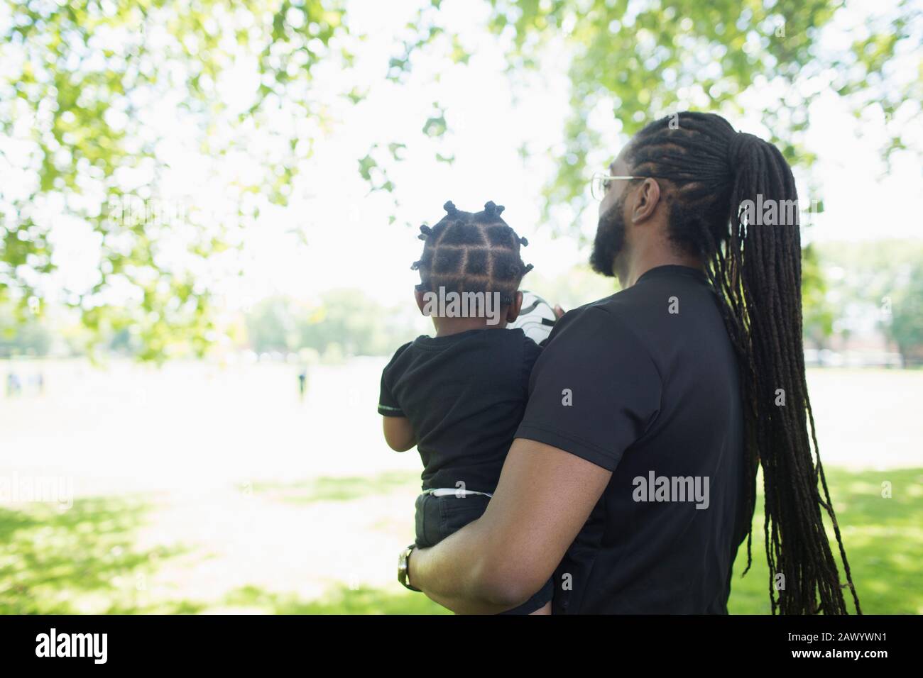 Father with long braids carrying son in park Stock Photo
