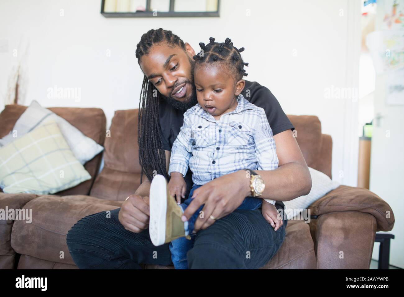 Father putting shoes on toddler son on sofa Stock Photo